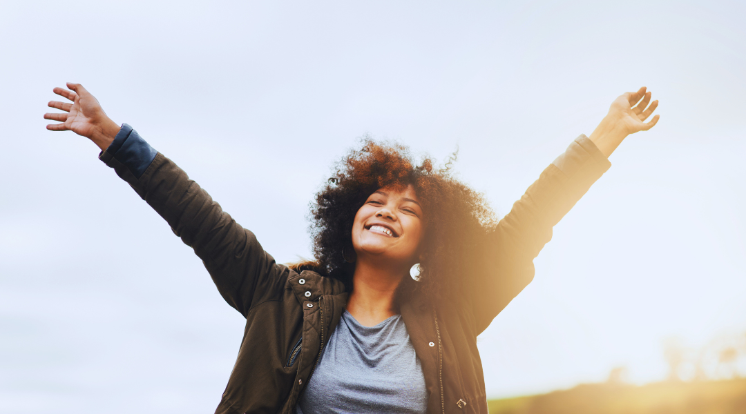 An image of a woman very happy with her arms in the air feeling relaxed outdoors in the sun