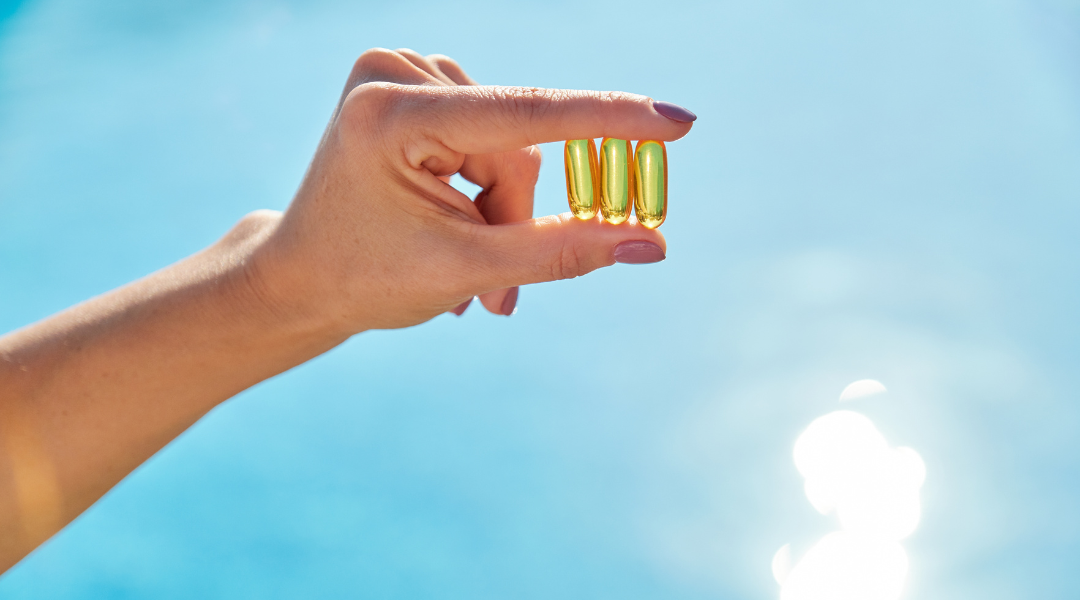 Hand in the sun holding 3 supplement tablets of vitamin d in front of the sun light