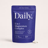 A blue stand-up pouch labeled 'Daily. 5 in 1 Magnesium Complex' on a light beige background, with two white capsules placed in front.